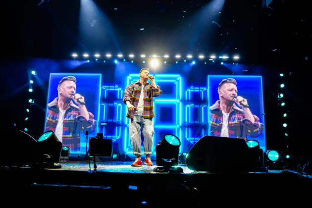 Ben Zucker steht mit Mikrofon auf der Bühne vor LED-Leinwänden mit seiner Projektionsaufnahme bei der Schlagernacht des Jahres in der LANXESS arena. Köln, 09.05.2026 NRW DE