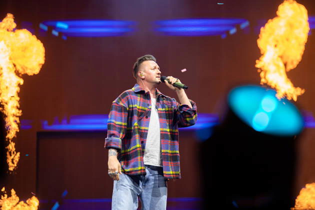 Ben Zucker steht mit Mikrofon auf der Bühne und wird von Feuer-Effekten umgeben während der Schlagernacht des Jahres 2026. Köln, Lanxess Arena NRW DE