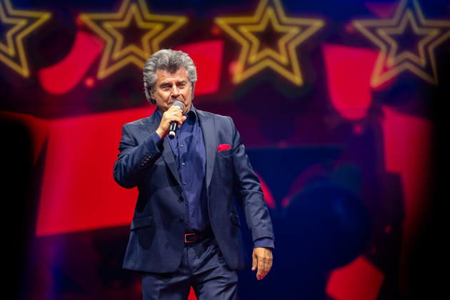 RECORD DATE NOT STATED Andy Borg steht mit Mikrofon in der Hand auf der Bühne, im Hintergrund sind dekorative gelbe Sterne vor rotem Hintergrund zu sehen. Köln, Lanxess Arena NRW DE