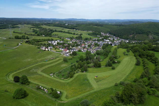Luftaufnahme. Fruehling (Frühling) im Siegerland. Eine saftig gruene (grüne) Wiese wird im Vordergrund von einem Traktor mit einem Maehwerk (Mähwerk) gemaeht (gemäht). Im Hintergrund der Ort Siegen-Oberschelden. Fruehling (Frühling) im Siegerland am 23.05.2026 in Siegen Deutschland.