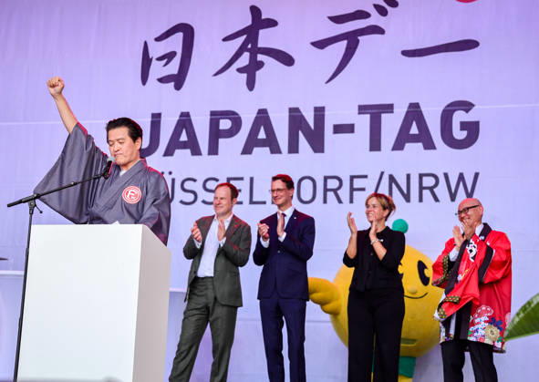 Japan-Tag 2026 in Düsseldorf, einzigartiges Kulturfest in der Landeshauptstadt von NRW - Takao Hariya, Präsident des japanischen Clubs in Düsslddorf bei seienr Begrüssungsrede - im Hitergrund stehen NRW Ministerpräsident Hendrik Wüst, NRW Ministerin für Wirtschaft und Kultur Mona Neubaur und der japanische Generalkonsul für Düsseldorf Yoshitaka Tsunoda überraschte die Zuschauer als bekennender Fan von Fortuna Düsseldorf - im Hintergrund Applaus von Düsseldorfs OB Dr. Stephan Keller, NRW Ministerpräsident Hendrik Wüst, NWR Wirtschafts & Kultur Ministerin Mona Neubaur und dem japanischen Generalkonsul für Düsseldorf Yoshotaka Tsunoda auf der Bühne... Düsseldorf Burgplatz NRW Deutschland