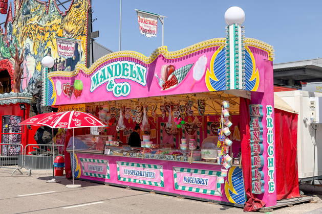 Freiburg im Breisgau GER, Volksfest, Freiburg im Breisgau, 24.05.2026 Ein bunter Süßwarenstand mit der Aufschrift Mandeln & Co bietet Schokofrüchte, Nussspezialitäten und Magenbrot auf einem Jahrmarkt an. Im Hintergrund ist eine Jahrmarktattraktion mit gruseligen Motiven zu erkennen. Copyright: xEibner-Pressefoto ThomasxHessx
