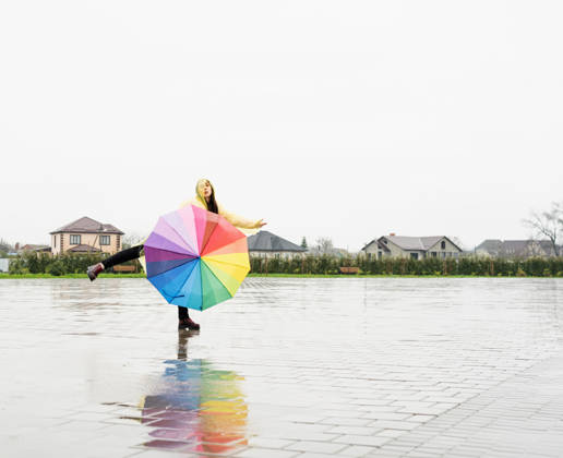 Eine schöne brünette Frau, die einen bunten Regenschirm hält und im Regen tanzt Beautiful brunette woman in yellow raincoat holding rainbow umbrella out in the rain (License=RF) ,model released, Symbolfoto Copyright: xZoonar.com ILONAxSHOROKHOVAx 25077121 ,model released, Symbolfoto ,property released