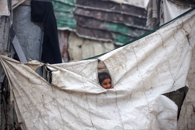 Palestinian Muslims Attend The Eid Al-Adha Prayer, In Gaza City A displaced Palestinian girl peers through a tear in a tent wall as members of Palestinian Islamic Jihad stand on a street during Eid al-Adha in Gaza City, on May 27, 2026. Gaza Palestine  Copyright: xMajdixFathix originalFilename: fathi-notitle260527_npV33.jpg