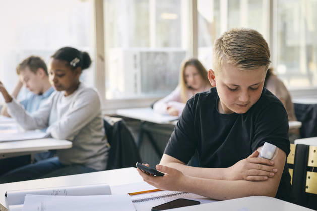 Junior high school student checking blood sugar level through glucose meter while sitting at desk with books in classroo Sweden, Stockholm, model released, property released Copyright: xMaskotx , MA125503 MA125503