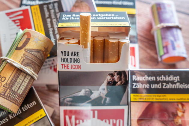 Mehrere Zigarettenschachtelen neben Euro Geldschein symbolisiert die finanziellen Auswirkungen des Rauchens. Das Bild steht für Tabaksteuer, mögliche Steuererhöhungen, steigende Zigarettenpreise und höhere Ausgaben für Verbraucher.