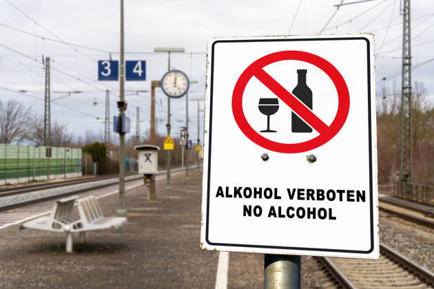 FOTOMONTAGE, Schild am Bahnhof: ALKOHOL VERBOTEN, NO ALCOHOL. Die Deutsche Bahn (DB) führt schrittweise ein bundesweites Alkoholkonsumverbot an ihren Bahnhöfen ein. Das Verbot gilt für Bahnsteige und Bahnhofshallen, nicht jedoch für gastronomische Betriebe