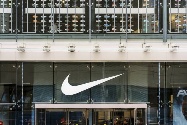 Das Äußere eines Nike Einzelhandelsgeschäfts mit einem großen weißen Nike Swoosh Logo auf Glasscheiben. In den Regalen im Geschäft sind auffällige farbenfrohe Sneaker angeordnet The exterior of a Nike retail store featuring a large white Nike Swoosh logo on glass panels, with a prominent display of colorful sneakers arranged on shelves inside the store Copyright: imageBROKER NadtochiyxPhotograph ibliqx18496506.jpg
