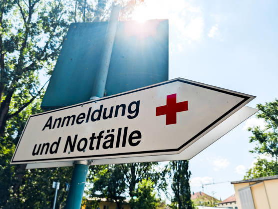 Wegweiser mit rotem Kreuz als Krankenhaus bzw. Medizin Symbol mit Aufschrift: Anmeldung und Notfälle