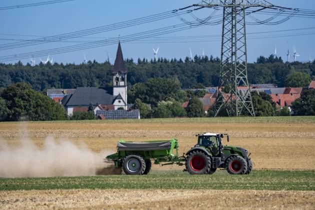 Trecker mit Mineraldüngerstreuer, bearbeitet ein abgeerntetes Getreidefeld, streut mineralischen Dünger, Kalk aus, um die Qualität des Boden für eine erneute Nutzung, Aussaat zu steigern, bei Marsberg-Meerhof, NRW, Deutschland Feldarbeit