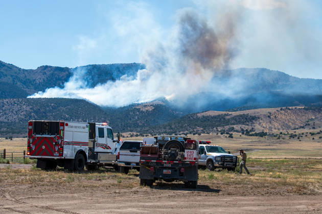 August 23, 2026, Elberta, Utah, USA: A plume of thick smoke rises into the sky above a mountain ridge as the Big Mountain Fire burns southwest of Elberta, Utah, United States, on August 23, 2026. A line of emergency response vehicles can be seen staged along a dirt road below the active wildland blaze. Elberta USA - ZUMAm292 20260823_znp_m292_003 Copyright: xCharlesxMcClintockxWilsonx