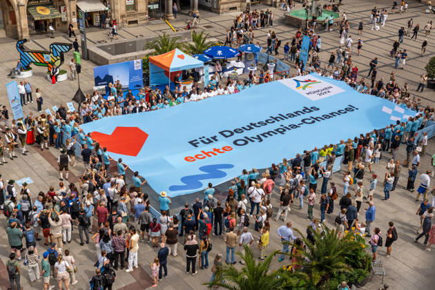 Für Deutschlaands echte Olympia-Chance! Münchner Olympia-Bewerbung mit Riesen-Banner, Marienplatz, München, 26. August 2026 Deutschland, München, 26. August 2026, Für Deutschlaands echte Olympia-Chance! Münchner Olympia-Bewerbung mit 20 x 10 Mweter großem Banner und einem Riesen-Dackel (links oben), Marienplatz, Panorama, Countdown zur Entscheidung des Deutschen Olympischen Sportbunds, in genau einem Monat, Bayern