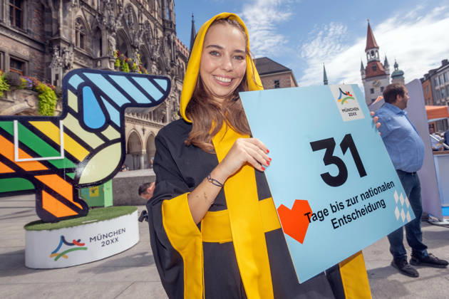 Münchner Kindl Sina Hochreiter mit Schild: 31 Tage bis zur nationalen Entscheidung, Münchner Olympia-Bewerbung mit Riesen-Dackel, Marienplatz, München, 26. August 2026 Deutschland, München, 26. August 2026, Münchner Kindl Sina Hochreiter, 27, mit Schild: 31 Tage bis zur nationalen Entscheidung, Münchner Olympia-Bewerbung mit drei Meter hohem Riesen-Dackel (links), Marienplatz, Countdown bis zur Entscheidung des Deutschen Olympischen Sportbunds, in genau einem Monat, Bayern