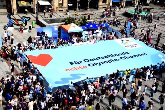Olympiade Symbol Banner Muenchen 26.08.2026 Marienplatz vor Symbol Olympia Waldi Oberbürgermeister Dominik Krause Wirtschaftsreferent Dr. Christian Scharpf geben gemeinsam mit Wolfram Hatz, Präsident der Vereinigung der Bayerischen Wirtschaft, und dem IHK-Regionalausschuss-den David Boppert als Vertretern des Bündnisses PRO Olympia den schuss für den Countdown zur Entscheidung des Deutschen Sportbunds, welcher Kandidat für Deutschland ins internationale um die Austragung der Olympischen und Paralympischen Sommerspiele ab 2036 geht. Foto Muenchen