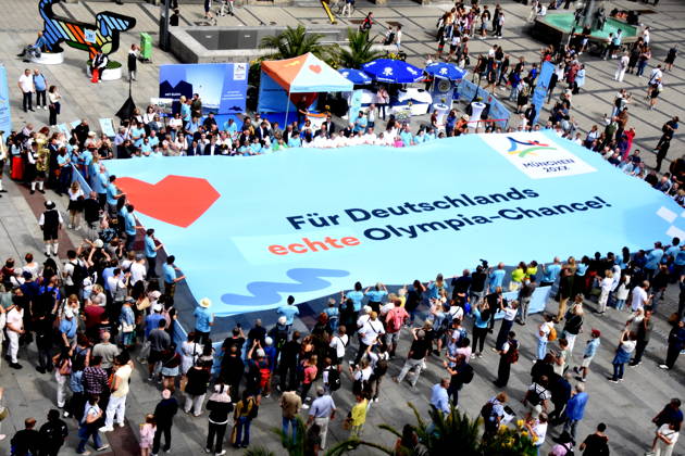 Olympiade Symbol Banner Muenchen 26.08.2026 Marienplatz vor Symbol Olympia Waldi Oberbürgermeister Dominik Krause Wirtschaftsreferent Dr. Christian Scharpf geben gemeinsam mit Wolfram Hatz, Präsident der Vereinigung der Bayerischen Wirtschaft, und dem IHK-Regionalausschuss-den David Boppert als Vertretern des Bündnisses PRO Olympia den schuss für den Countdown zur Entscheidung des Deutschen Sportbunds, welcher Kandidat für Deutschland ins internationale um die Austragung der Olympischen und Paralympischen Sommerspiele ab 2036 geht. Foto Muenchen
