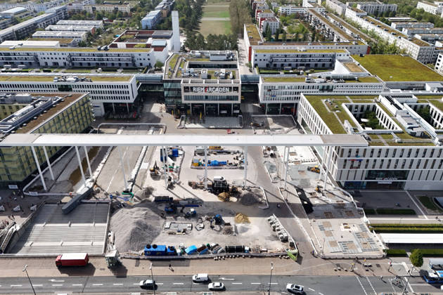 Umgestaltung des Willy-Brandt-Platzes an den Riem Arcaden: Versiegelte Flaechen werden in Gruenflaechen umgewandelt. Am Willy-Brandt-Platz vor den Riem Arcaden in Muenchen laufen die Bauarbeiten zur Neugestaltung. Im Zuge der Umgestaltung sollen bisher versiegelte Flaechen entsiegelt und durch Gruenflaechen ersetzt werden. Baustellenabsperrungen, Baumaterial und ein Radlader praegen derzeit das Bild des Platzes.