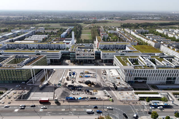 Umgestaltung des Willy-Brandt-Platzes an den Riem Arcaden: Versiegelte Flaechen werden in Gruenflaechen umgewandelt. Am Willy-Brandt-Platz vor den Riem Arcaden in Muenchen laufen die Bauarbeiten zur Neugestaltung. Im Zuge der Umgestaltung sollen bisher versiegelte Flaechen entsiegelt und durch Gruenflaechen ersetzt werden. Baustellenabsperrungen, Baumaterial und ein Radlader praegen derzeit das Bild des Platzes.