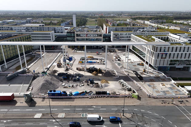 Umgestaltung des Willy-Brandt-Platzes an den Riem Arcaden: Versiegelte Flaechen werden in Gruenflaechen umgewandelt. Am Willy-Brandt-Platz vor den Riem Arcaden in Muenchen laufen die Bauarbeiten zur Neugestaltung. Im Zuge der Umgestaltung sollen bisher versiegelte Flaechen entsiegelt und durch Gruenflaechen ersetzt werden. Baustellenabsperrungen, Baumaterial und ein Radlader praegen derzeit das Bild des Platzes.