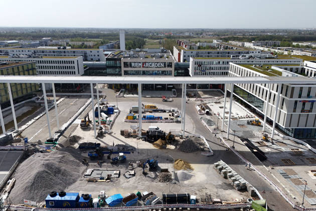 Umgestaltung des Willy-Brandt-Platzes an den Riem Arcaden: Versiegelte Flaechen werden in Gruenflaechen umgewandelt. Am Willy-Brandt-Platz vor den Riem Arcaden in Muenchen laufen die Bauarbeiten zur Neugestaltung. Im Zuge der Umgestaltung sollen bisher versiegelte Flaechen entsiegelt und durch Gruenflaechen ersetzt werden. Baustellenabsperrungen, Baumaterial und ein Radlader praegen derzeit das Bild des Platzes.