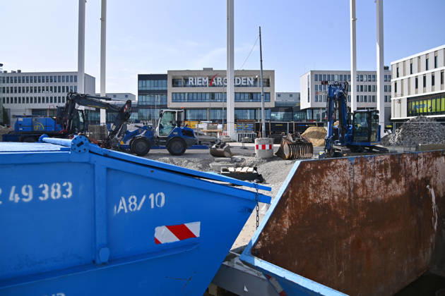 Umgestaltung des Willy-Brandt-Platzes an den Riem Arcaden: Versiegelte Flaechen werden in Gruenflaechen umgewandelt. Am Willy-Brandt-Platz vor den Riem Arcaden in Muenchen laufen die Bauarbeiten zur Neugestaltung. Im Zuge der Umgestaltung sollen bisher versiegelte Flaechen entsiegelt und durch Gruenflaechen ersetzt werden. Baustellenabsperrungen, Baumaterial und ein Radlader praegen derzeit das Bild des Platzes.