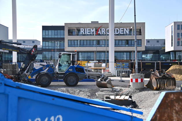 Umgestaltung des Willy-Brandt-Platzes an den Riem Arcaden: Versiegelte Flaechen werden in Gruenflaechen umgewandelt. Am Willy-Brandt-Platz vor den Riem Arcaden in Muenchen laufen die Bauarbeiten zur Neugestaltung. Im Zuge der Umgestaltung sollen bisher versiegelte Flaechen entsiegelt und durch Gruenflaechen ersetzt werden. Baustellenabsperrungen, Baumaterial und ein Radlader praegen derzeit das Bild des Platzes.