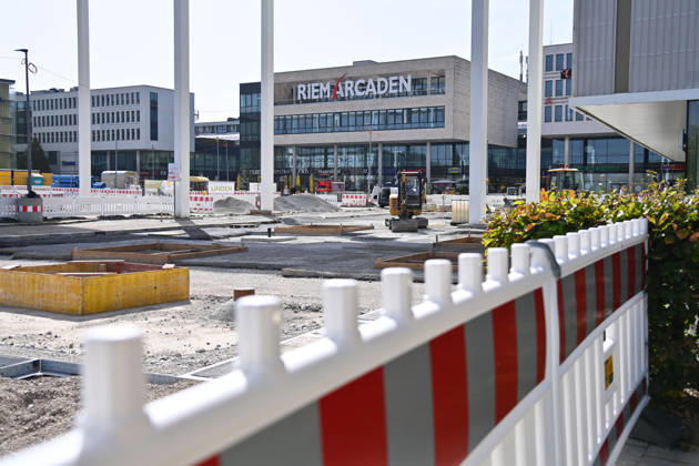 Umgestaltung des Willy-Brandt-Platzes an den Riem Arcaden: Versiegelte Flaechen werden in Gruenflaechen umgewandelt. Am Willy-Brandt-Platz vor den Riem Arcaden in Muenchen laufen die Bauarbeiten zur Neugestaltung. Im Zuge der Umgestaltung sollen bisher versiegelte Flaechen entsiegelt und durch Gruenflaechen ersetzt werden. Baustellenabsperrungen, Baumaterial und ein Radlader praegen derzeit das Bild des Platzes.