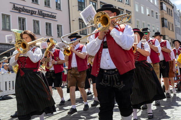 Traditioneller Plärrerumzug in Augsburg. Eine bayerische Musikkapelle in Tracht zieht beim traditionellen Plärrerumzug durch Augsburg durch die Innenstadt. Musiker in Lederhosen und Dirndl begleiten den Festzug mit Blasmusik