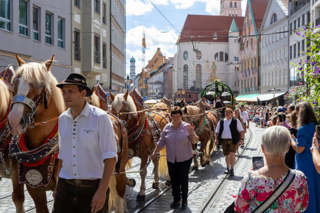 Traditioneller Plärrerumzug in Augsburg. Ein traditionelles Pferdegespann mit geschmückten Kaltblütern und Festwagen zieht beim Plärrerumzug durch die Augsburger Innenstadt. Zahlreiche Zuschauer säumen die Strecke des Festzugs