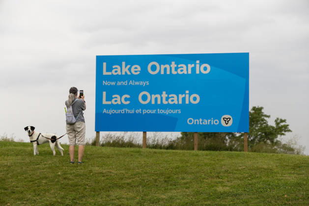 (260830) -- HAMILTON, Aug. 30, 2026 -- A woman takes photos of an English-French bilingual sign reading Lake Ontario Now and Always at a lakeside conservation area in Hamilton, Ontario, Canada, on Aug. 30, 2026. Canadian Prime Minister Mark Carney said Thursday that the name Lake Ontario carries a long history and that Canadians will always use this name regardless of external changes. The Canadian prime minister made the remarks after U.S. President Donald Trump signed an executive order earlier on Thursday, directing the Department of the Interior to rename the lake Lake America, as trade tensions between the United States and Canada have been escalating. (Photo by Xinhua) CANADA-ONTARIO-HAMILTON-LAKE ONTARIO-NAME ZouxZheng 