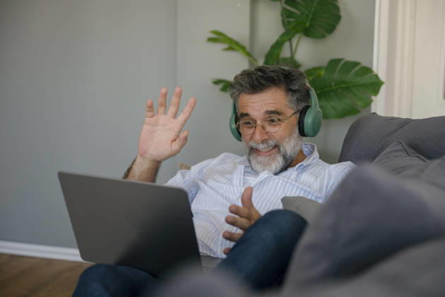 Smiling man wearing headphones using laptop for video call on couch model released, Symbolfoto property released, FLMZF02934