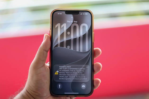 Deutschland, Europa. Nahaufnahme eines Smartphones in der Hand mit einer angezeigten Testwarnung zum bundesweiten Warntag. Auf dem Sperrbildschirm sind die Warnmeldungen des Bundesamtes für Bevölkerungsschutz und Katastrophenhilfe (BBK) sowie Uhrzeit und Datum sichtbar. Symbolbild zu Katastrophenschutz, Cell Broadcast, Warnsystemen, Bevölkerungsschutz und Notfallkommunikation. Copyright: xAymanxAlahmedx