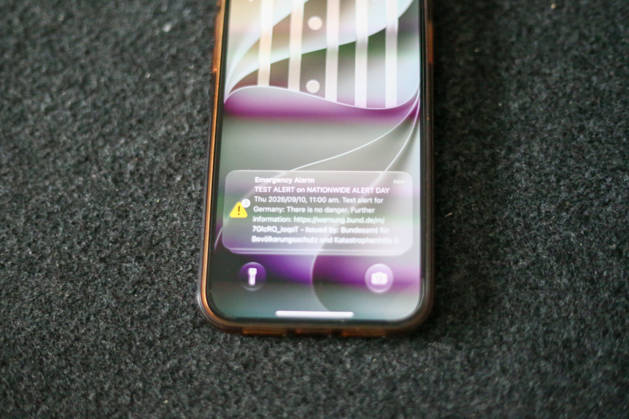 Deutschland, Europa. Smartphone liegt auf einer dunklen Oberfläche und zeigt auf dem Sperrbildschirm eine Testwarnung zum bundesweiten Warntag. Die Cell-Broadcast-Warnmeldung des Bundesamtes für Bevölkerungsschutz und Katastrophenhilfe (BBK) ist auf dem Display sichtbar. Symbolbild zu Notfallwarnsystemen, Bevölkerungsschutz, Krisenvorsorge, digitaler Kommunikation und öffentlicher Sicherheit. Copyright: xAymanxAlahmedx