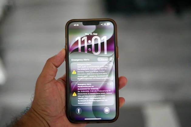 Deutschland, Europa. Nahaufnahme eines Smartphones in der Hand mit einer angezeigten Testwarnung zum bundesweiten Warntag. Auf dem Sperrbildschirm sind die Warnmeldungen des Bundesamtes für Bevölkerungsschutz und Katastrophenhilfe (BBK) sowie Uhrzeit und Datum sichtbar. Symbolbild zu Katastrophenschutz, Cell Broadcast, Warnsystemen, Bevölkerungsschutz und Notfallkommunikation. Copyright: xAymanxAlahmedx