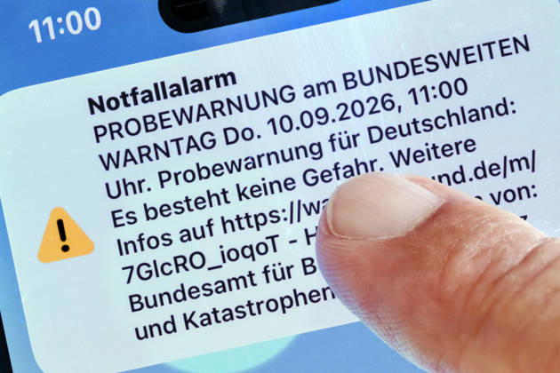 Bundesweiter Warntag, Probealarm um 11 Uhr, Warnmeldung auf dem Smartphone, 10. September 2026 Deutschland, München, 10. September 2026, bundesweiter Warntag, Warnmeldung um 11 Uhr auf einem Smartphone Bildschirm, Katastrophen-Warnsystem, Notfallalarm für den Ernstfall, das Bundesamt für Bevölkerungsschutz und Katastrophenhilfe (BBK) verschickt Push-Nachrichten per Cell Broadcast, Funktionsfähigkeit der Warnsysteme werden überprüft, Smartphone-Nutzer werden als Test über Gefahren und Katastrophen gewarnt, keine Gefahr, Katastrophenschutz, FOTOMONTAGE aus zwei eigenen Bildern, Handy und Finger,