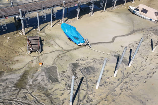 Wetterfeature, Bei sonnigem Spätsommerwetter am Bodensee liegen einige Boote aufgrund des niedrigen Wasserstands auf dem Trockenen. Gleichzeitig zeigt sich der Bodensee von seiner malerischen Seite das Wasser schimmert bei strahlendem Sonnenschein grünlich-blau, während sich die Uferlandschaft unter nahezu wolkenlosem Himmel präsentiert. (Aufnahme mit einer Drohne) Moos Baden-Württemberg Deutschland Moos