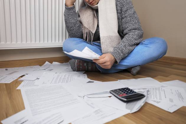 Ein Mann mit Schal sitzt mit Rechnungen und einem Taschenrechner neben dem Heizkörper auf dem Boden und macht sich Sorgen wegen der hohen Heizkosten A man wearing a scarf sits on the floor with bills and a calculator next to the radiator and is worried about the high heating costs Copyright: imageBROKER KyryloxSyvun ibxiqx18688159.jpg ,model released, Symbolfoto ,property released