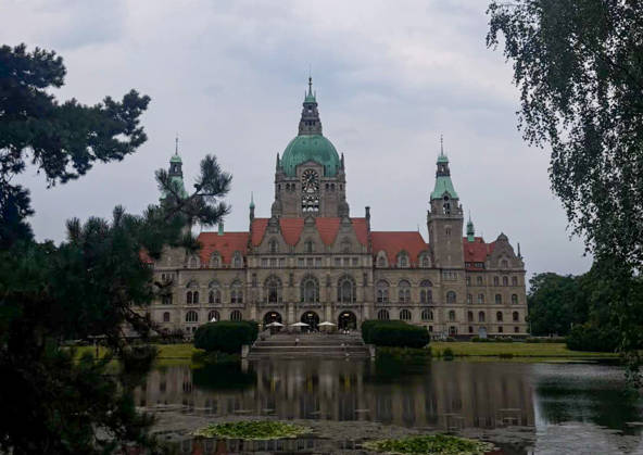 Hannover, Niedersachsen, Deutschland, Europa. Das Neue Rathaus von Hannover spiegelt sich im Maschteich. Die historische Rathausfassade mit ihrer markanten Kuppel und den Türmen ist von Parkanlagen und Bäumen eingerahmt. Im Vordergrund befindet sich der Teich mit Wasserpflanzen und Spiegelungen. Dokumentarische Aufnahme eines bekannten Wahrzeichens der Landeshauptstadt Hannover. Copyright: xAymanxAlahmedx