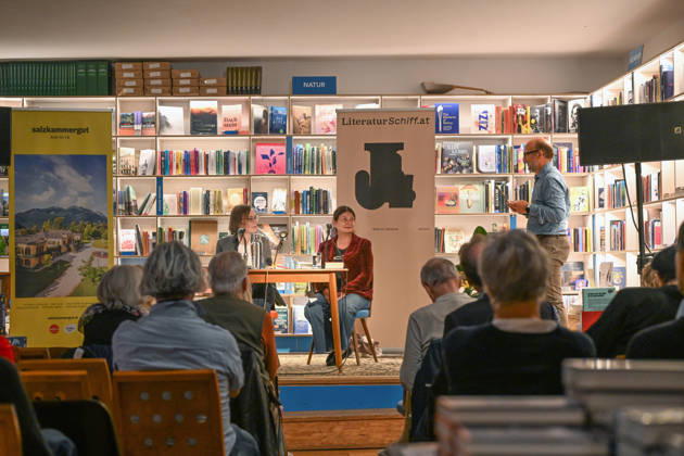 Minifestival AH0J (Literaturfestival) - Tschechien setzt über - der Kulturinitiative Literaturschiff, in der Buchhandlung Kurdirektion in Bad Ischl. Lesungen und Gespräche in Korrespondenz zum Gastauftritt Tschechiens auf der Frankfurter Buchmesse 2026. Es liest die tschechische Schriftstellerin und mehrfache Literaturpreisträgerin Radka Denemarkovich. Die Veranstaltung wrd moderiert von Julia Miesenböck, fotografiert am 30.09.26. Das Bild zeigt den Veranstalter Christian Gsöllradl-Samhabber, der die Schriftstellerin Radka Denemarkovic und die Moderatorin Julia Miesenböck (links) begrüßt 2026 - Minifestival AH0J (Literaturfestival) - Tschechien setzt über - der Kulturinitiative Literaturschiff, in der Buchhandlung Kurdirektion in B