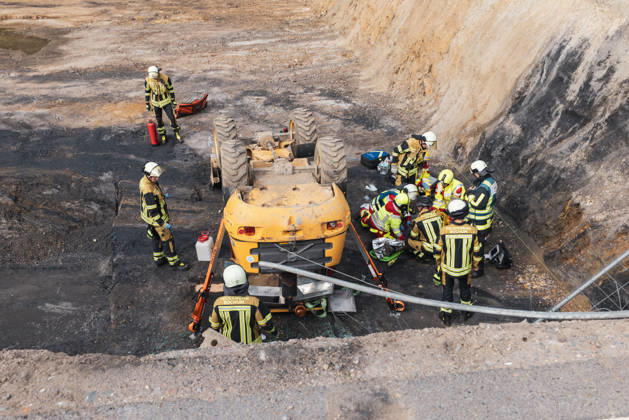 RECORD DATE NOT STATED Feuerwehr und Rettungsdienst versorgen eine Person neben einem umgestürzten Radlader in einer Baugrube an der Charlottenstraße in Bochum-Wiemelhausen. Die Baumaschine war etwa dreieinhalb bis vier Meter tief abgestürzt und auf dem Dach liegen geblieben. Einsatzkräfte sichern das Fahrzeug mit Stützen.