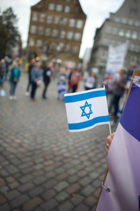 Flensburg, Schleswig-Holstein Flensburg gedenkt den Opfern des 7. Oktober 2023. Teilnehmer versammeln sich auf dem Südermarkt. Vorner Pserson hält Flagge von Israel. Es werden Lieder gesungen und die Namen und Geschichten einzelner Opfer des Terroranschlages vorgelesen. Aufnahme vom 07.10.2026, Flensburg