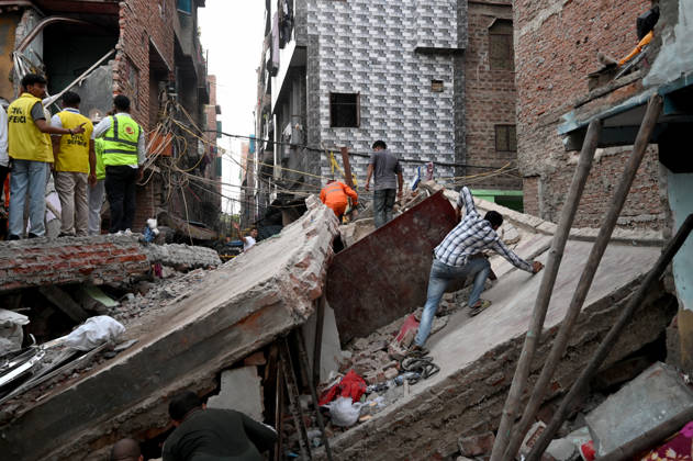 NEW DELHI, INDIA - OCTOBER 7: National Disaster Response Force (NDRF) jawans, Delhi Fire Service personnel, and local residents navigate heavy rubble during a search and rescue operation after a four-storey residential building collapsed in the New Seemapuri area of Shahdara on October 7, 2026, in New Delhi, India. The structural collapse occurred around 3:30 PM behind the local fish market, trapping multiple residents under concrete slabs and damaging two adjoining houses. At least one minor died while eight people were rescued and rushed to Rajiv Gandhi Super Speciality Hospital for emergency medical treatment as sniffer dogs and excavators worked late into the evening to locate remaining trapped survivors. (Photo by Ishant Chauhan Hindus