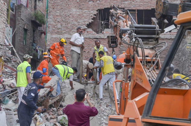 NEW DELHI, INDIA - OCTOBER 7: National Disaster Response Force (NDRF) jawans, Delhi Fire Service personnel, and local residents navigate heavy rubble during a search and rescue operation after a four-storey residential building collapsed in the New Seemapuri area of Shahdara on October 7, 2026, in New Delhi, India. The structural collapse occurred around 3:30 PM behind the local fish market, trapping multiple residents under concrete slabs and damaging two adjoining houses. At least one minor died while eight people were rescued and rushed to Rajiv Gandhi Super Speciality Hospital for emergency medical treatment as sniffer dogs and excavators worked late into the evening to locate remaining trapped survivors. (Photo by Raj K Raj Hindustan T