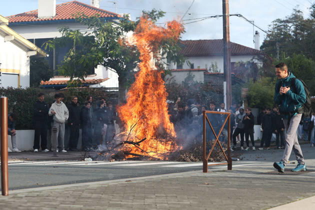 October 8, 2026, Anglet, Nouvelle Aquitaine, France: Flames rise from a large pile of burning branches on a residential street near the Cantau high school in Anglet, southwestern France, as dozens of students watch from the pavement and a man walks past in the foreground, during a student protest against overcrowded classrooms, teacher shortages and school underfunding. Anglet France - ZUMAb298 20261008_zsp_b298_004 Copyright: xJulesxBuonx