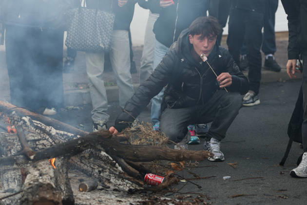 October 8, 2026, Anglet, Nouvelle Aquitaine, France: A high school student crouches by the embers of a fire of branches burning on the road and blows on a marshmallow on a stick outside the Cantau high school in Anglet, southwestern France, during a student protest against overcrowded classrooms, teacher shortages and school underfunding. Anglet France - ZUMAb298 20261008_zsp_b298_007 Copyright: xJulesxBuonx