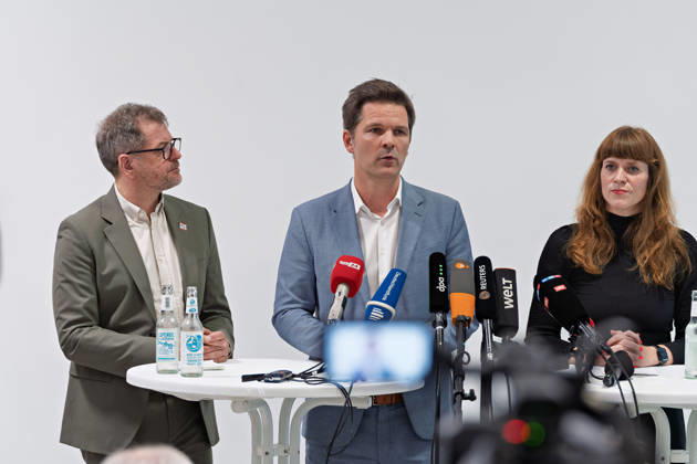 Berlin, 08.10.2026: Steffen Krach (SPD, M.) spricht neben Werner Graf (Bündnis 90 Die Grünen, l.) und Kerstin Wolter-Ehling (Die Linke, r.) beim gemeinsamen Pressestatement nach Abschluss der Vorgespräche ihrer Parteien im Foyer des Hauses der Statistik, im Vordergrund Kameras der Medien. Pressestatement von Linke, Grünen und SPD in Berlin