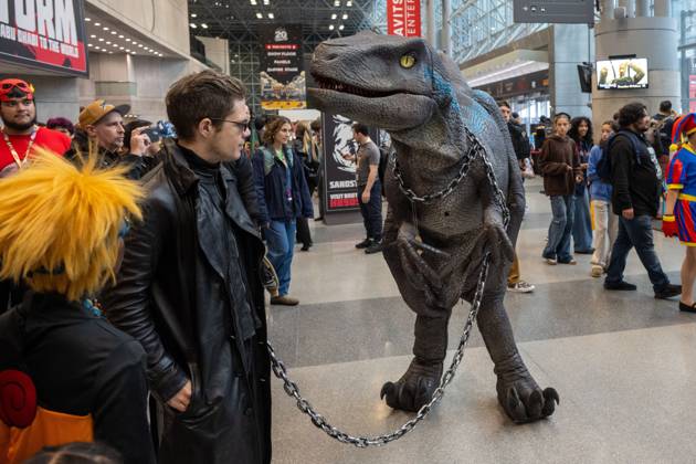 October 11, 2026, New York, New York, United States: A cosplayer dressed in a long black leather coat and dark sunglasses posing alongside a person in a realistic animatronic Velociraptor costume (resembling Blue from Jurassic World).during New York Comic Con 2026 at The Jacob K. Javits Convention Center on October 11, 2026 in New York City. New York United States - ZUMAs197 20261011_aaa_s197_358 Copyright: xRonxAdarx