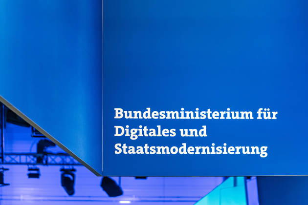 Berlin, 13.10.2026: Der Schriftzug Bundesministerium für Digitales und Staatsmodernisierung an einem blauen Deckenaufbau über dem Messestand des Ministeriums auf der Smart Country Convention. Das 2025 gegründete Ministerium unter Karsten Wildberger soll die Digitalisierung des Staates bündeln. Die Smart Country Convention (SCCON) ist die Kongressmesse für die Digitalisierung des öffentlichen Sektors und wird vom Digitalverband Bitkom gemeinsam mit der Messe Berlin veranstaltet. Vom 13. bis 15. Oktober 2026 treffen sich auf dem Berliner Messegelände Vertreter aus Bund, Ländern und Kommunen mit Unternehmen der Digitalwirtschaft, um über digitale Verwaltung, Smart City und digitale Souveränität zu diskutieren. Schriftzug des B