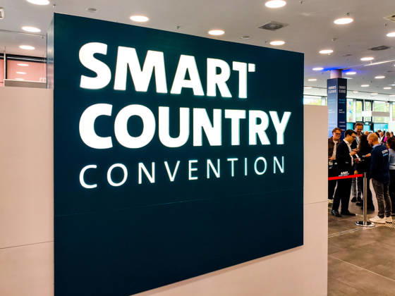 Grosses beleuchtetes Logo der Smart Country Convention (SCCON) im Eingangsbereich der Messe Berlin. Besucher und Fachpublikum stehen am Einlass der Kongressmesse. Smart Country Convention, SCCON 2026, Berlin, Messe, Digitalisierung, Digitalpolitik, Smart City, Smart Country, öffentliche Verwaltung, E-Government, digitale Transformation, IT, Technologie, Wirtschaft, Innovation, Kongress, Fachmesse, Besucher, Registrierung, Eingang, Veranstaltungslogo. Copyright: xJulianxCunowx