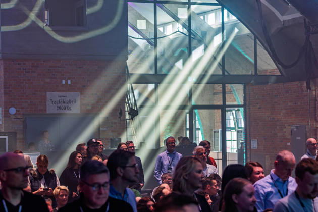 Berlin, 16.10.2026: Teilnehmerinnen und Teilnehmer der NeulandPro Connect 2026 verfolgen das Programm in der Backsteinhalle des WECC; Lichtstrahlen fallen durch den Nebel, ein altes Schild mit der Aufschrift Tragfähigkeit 2000 Kg erinnert an die frühere Nutzung des Gebäudes als Lagerhaus. Die zweitägige KI-Konferenz NeulandPro Connect 2026 findet am 16. und 17. Oktober im Westhafen Event & Convention Center (WECC) in Moabit statt, einem historischen Speichergebäude am Berliner Westhafen. Mit mehr als 50 Speakern sowie über 30 Workshops, Masterclasses und einem Hackathon richtet sich die Veranstaltung an Gründer, Führungskräfte, Unternehmen und KI-Interessierte. NeulandPro Connect 2026 - KI-Konferenz in Berlin