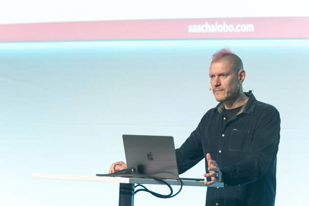 Berlin, 16.10.2026: Auf der NeulandPro Connect 2026 spricht der Publizist und Digital-Vordenker Sascha Lobo am Rednerpult zum Publikum. Die zweitägige KI-Konferenz NeulandPro Connect 2026 findet am 16. und 17. Oktober im Westhafen Event & Convention Center (WECC) in Moabit statt, einem historischen Speichergebäude am Berliner Westhafen. Veranstalter ist NeulandPro, eine Bildungs- und Medienmarke rund um Künstliche Intelligenz. Mit Vorträgen, Workshops und Hackathons richtet sich die Konferenz vor allem an kleine und mittelständische Unternehmen, Gründer und Führungskräfte, die KI praktisch einsetzen wollen; erwartet werden bis zu 1.000 Gäste. NeulandPro Connect 2026 - KI-Konferenz in Berlin